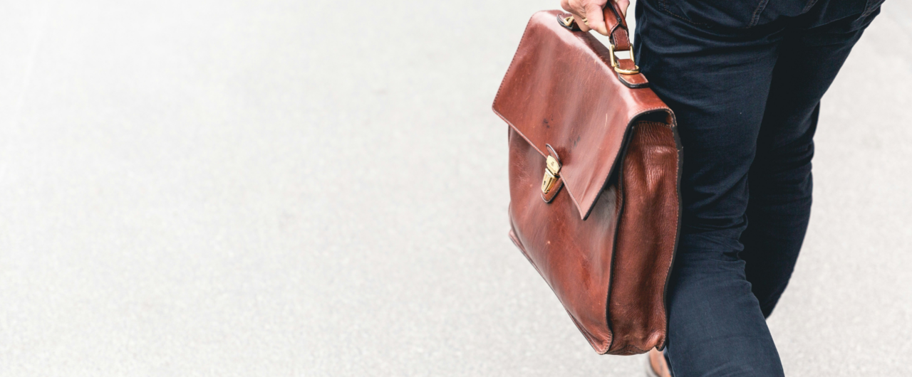 Ein Business-Profi trägt eine klassische braune Leder-Aktentasche im Gehen, symbolisch für Karriere, berufliche Mobilität und moderne Arbeitswelten im Kontext von Wirtschaft und Politik.