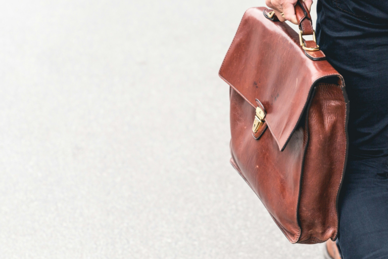 Ein Business-Profi trägt eine klassische braune Leder-Aktentasche im Gehen, symbolisch für Karriere, berufliche Mobilität und moderne Arbeitswelten im Kontext von Wirtschaft und Politik.